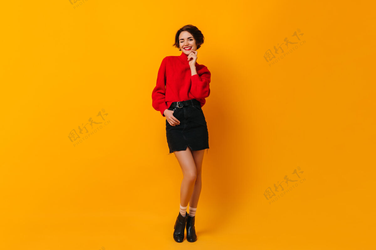 享受穿红毛衣的漂亮女人站在黄色的墙上服装魅力短发