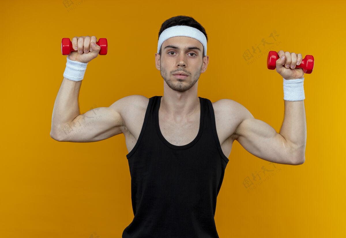 工作戴着头巾的年轻运动型男子 带着哑铃锻炼 严肃的脸庞凌驾于橙色之上哑铃长相脸