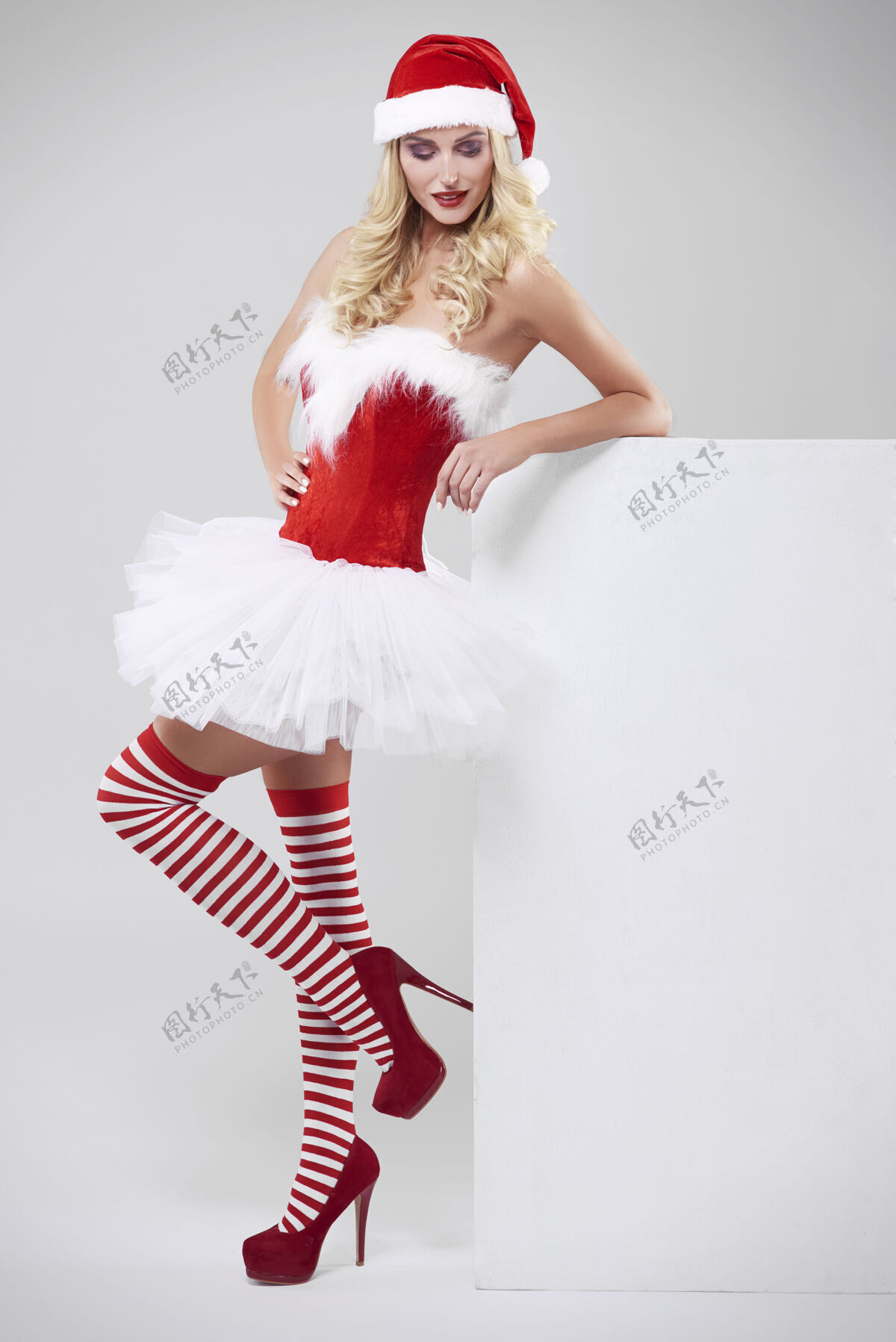 连衣裙灰墙上穿圣诞老人服装的性感女人站着严肃的抬起脚