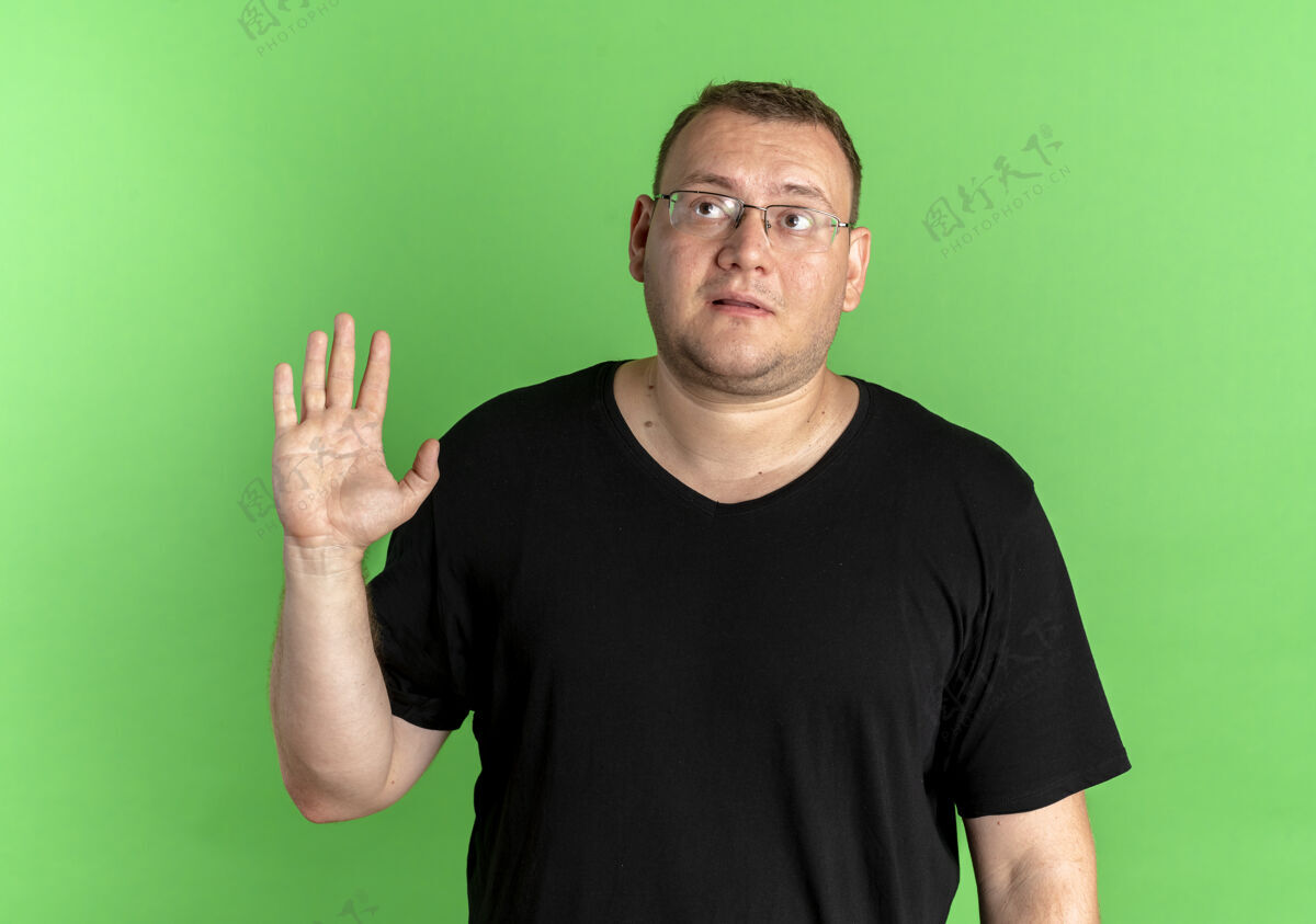 T恤戴眼镜的超重男子身穿黑色t恤 神情迷茫 挥舞着手中的绿色眼镜困惑看