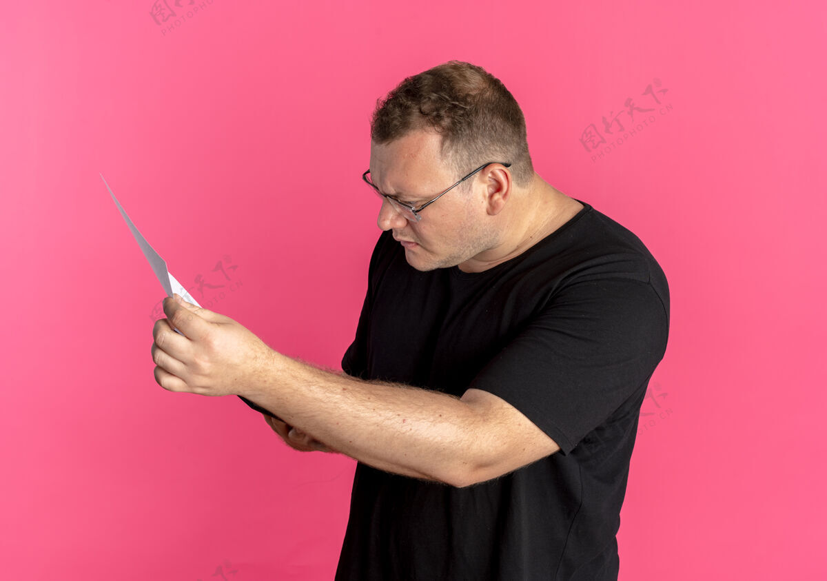 眼镜戴眼镜的超重男子穿着黑色t恤看着文件 严肃的脸超过了粉色黑色粉红色严重