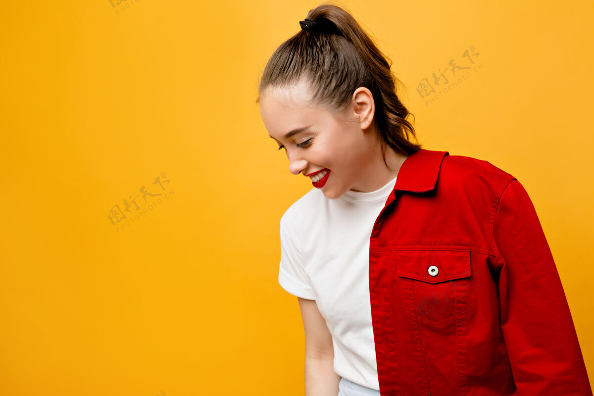 微笑黄色的墙上站着一个穿着红色夹克的快乐女孩在明亮的墙上摆着一张快乐的年轻女子心情愉快的室内照片护理可爱欢呼