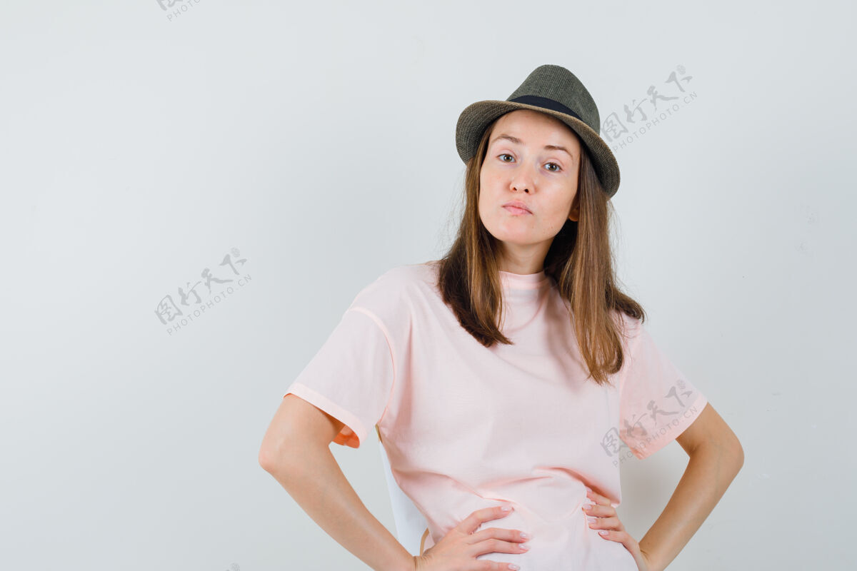 快乐年轻女孩手挽手放在腰上 穿着粉色t恤 戴着帽子 神情不悦 俯视前方年轻不高兴童年