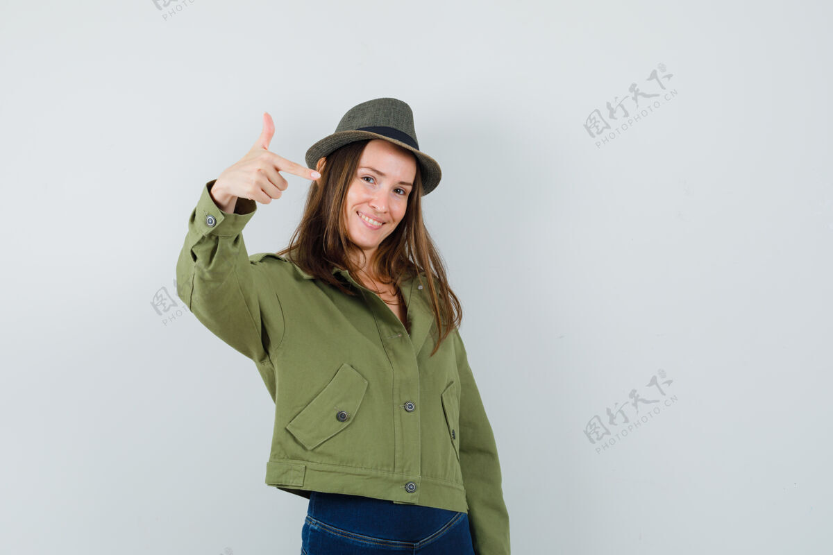 手指年轻女性在夹克 裤子 帽子上做手指手枪标志 看起来很自信正面图微笑年轻正面
