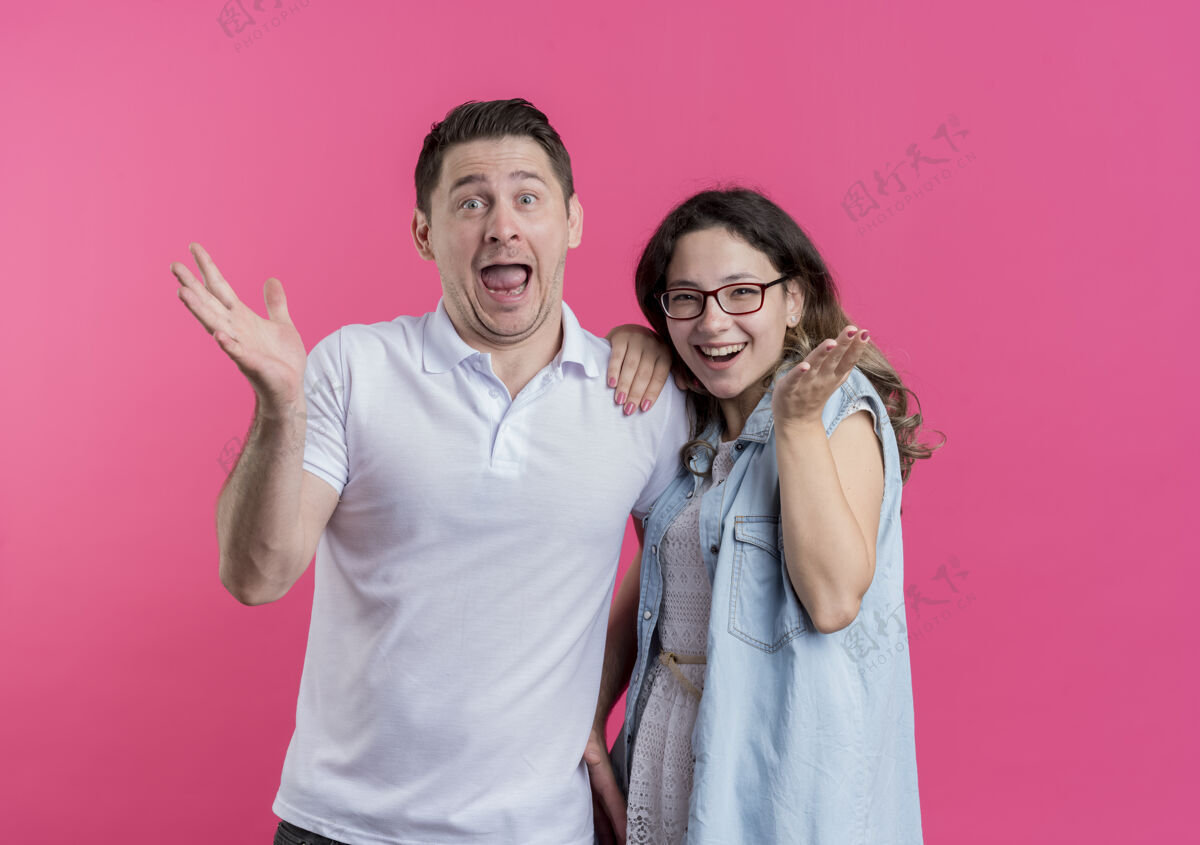 年轻一对穿着休闲服的年轻夫妇站在粉红色的墙上 面带微笑 既高兴又惊讶欢呼女人衣服