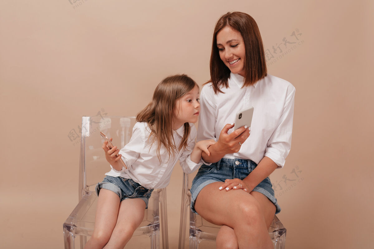 父母好奇的小女孩看着妈妈的手机 背景是有趣的米色手机女人肖像