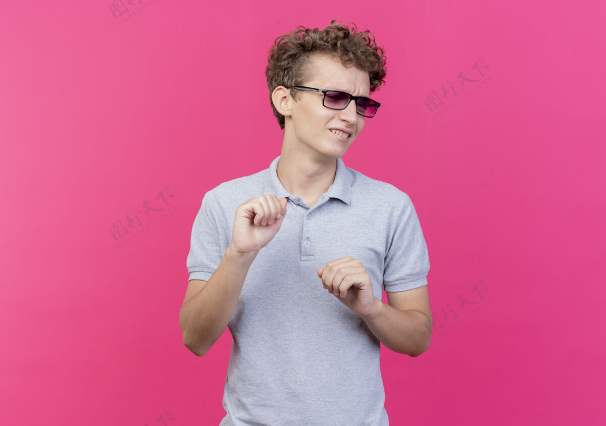 厌恶一个戴着黑眼镜 穿着灰色马球衫的年轻人站在粉色的墙上 带着厌恶的表情向一边看男人年轻表情