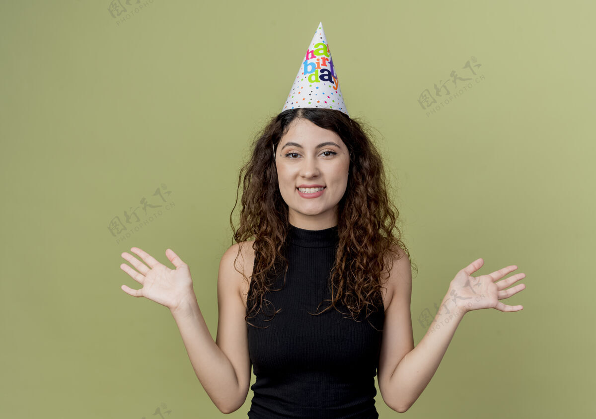光年轻漂亮的女人 卷发 戴着节日帽 站在光墙上 快乐而兴奋的生日派对概念帽子卷发看