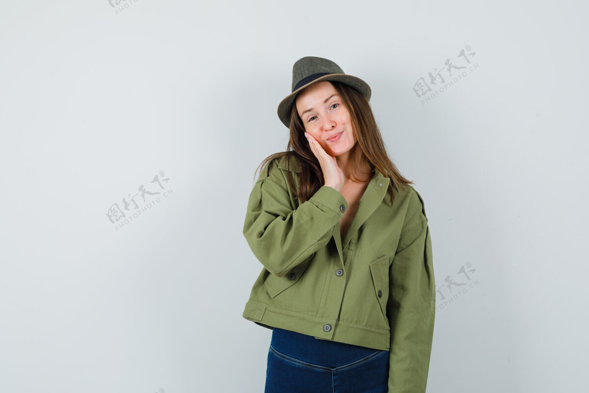 正面年轻女性穿着夹克 裤子 帽子 面颊靠在手掌上 看起来很可爱 前视图帽子漂亮瘦