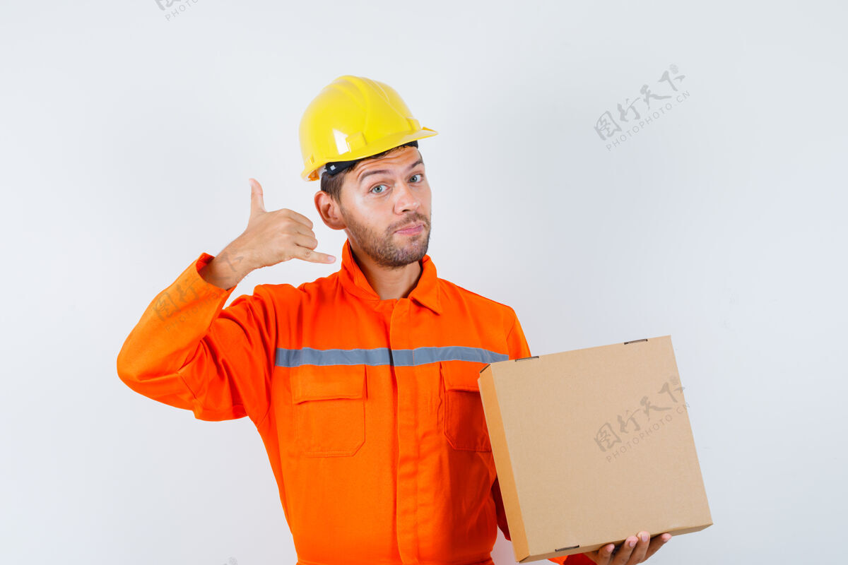 头盔建筑工人拿着纸板箱 穿着制服 戴着头盔 表情温和正面图职业手势建筑商
