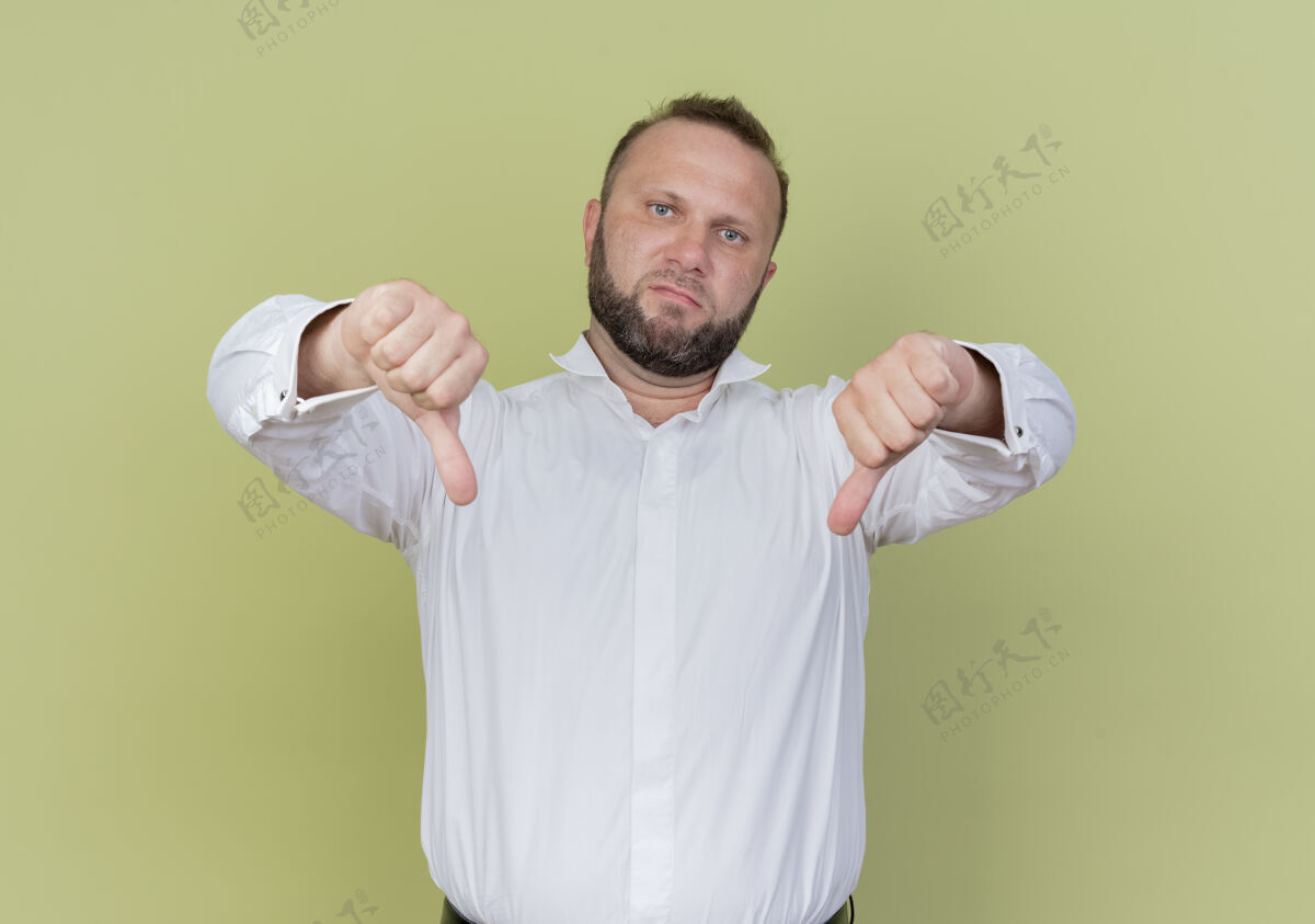 胡须穿着白衬衫的胡子男人不高兴地竖起大拇指站在轻墙上穿男人拇指