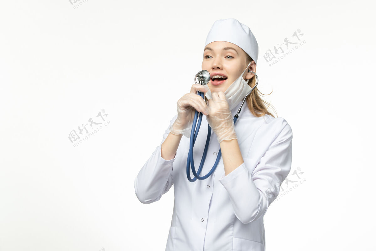 人员前视图：穿着白色医疗服的女医生在白色办公桌上使用听诊器疾病-流行性疾病肖像疾病医疗