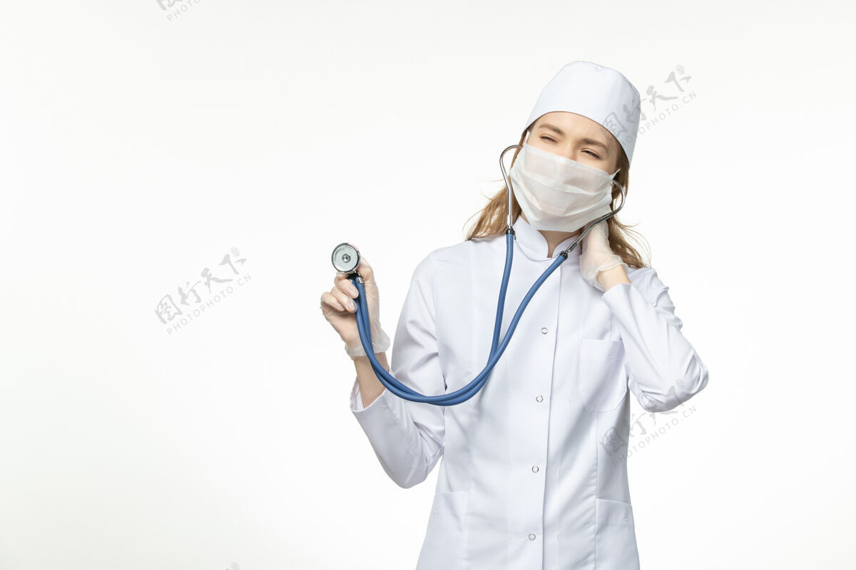 冠状病毒正面图女医生身穿医疗服戴口罩因冠状病毒手持听诊器对浅白壁病毒大流行冠状病毒-疾病病毒医疗器械冠状病毒预防