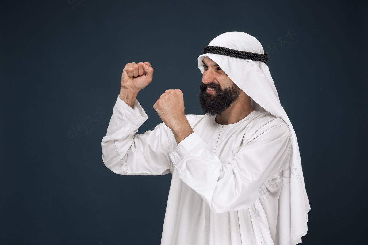 迪拜深蓝色空间上的阿拉伯沙特商人肖像年轻的男模站着 微笑着庆祝穆斯林男人人类