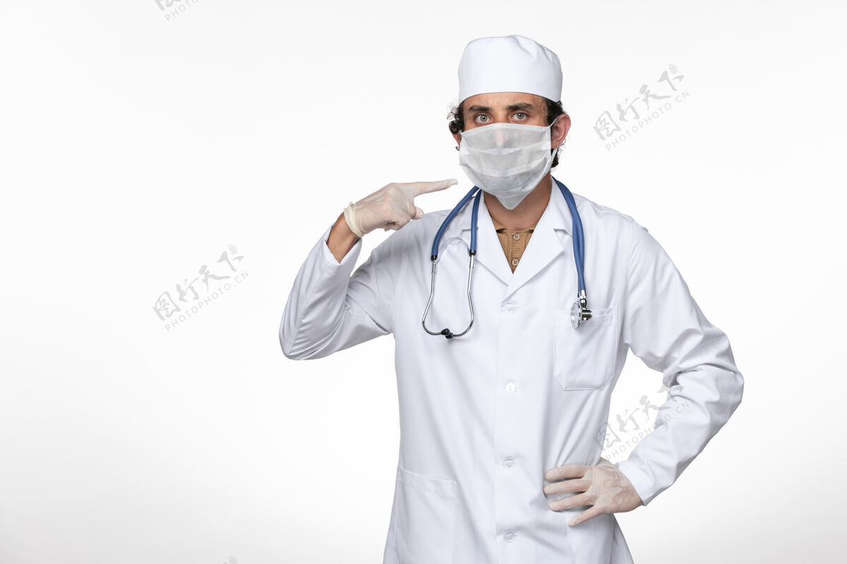 视图正面图身穿医疗服的男医生戴着口罩 以防柯维德-白墙病毒疾病柯维德-大流行大流行冠状病毒防护听诊器