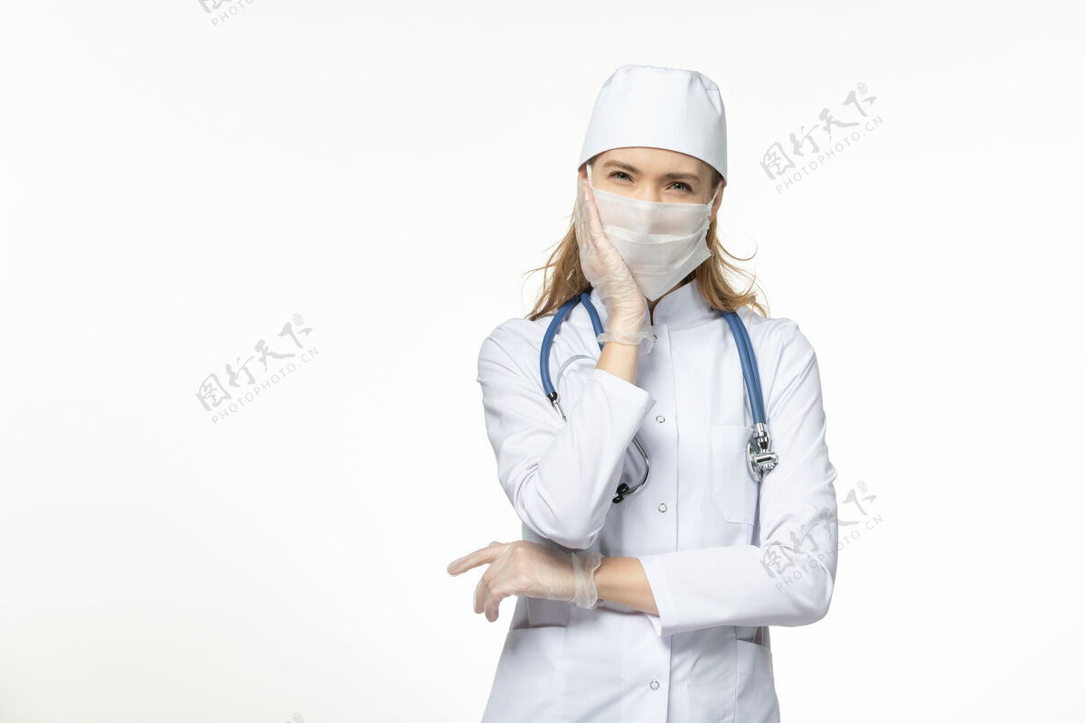 疾病正面图女医生穿着医疗服戴着口罩和手套因冠状病毒重压白墙大流行冠状病毒病疾病病毒大流行