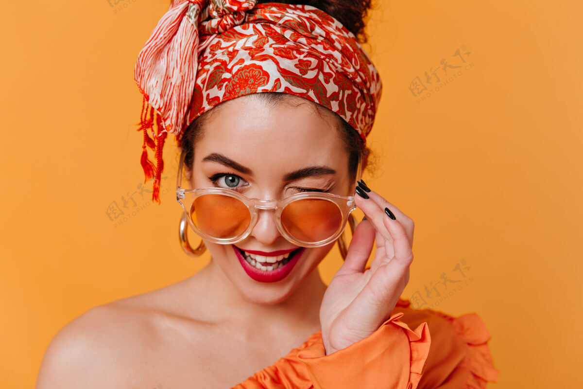 身体戴着非洲式大耳环和头带的可爱女人摘下橙色眼镜 风骚地眨着眼睛长裙现代红唇