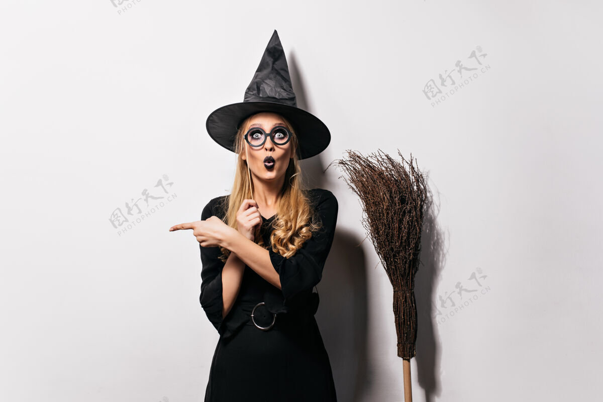 万圣节戴着眼镜的巫师站在白色的墙上滑稽的情绪巫师拿着帽子和扫帚摆姿势魔术师幽灵魔鬼