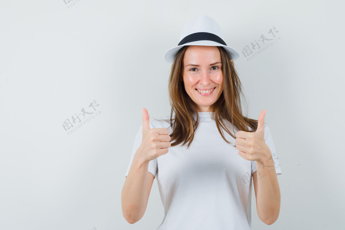 微笑穿着白色t恤 戴着帽子的年轻女孩向上竖起了大拇指 看上去很快乐 正前方的景色孩子漂亮快乐