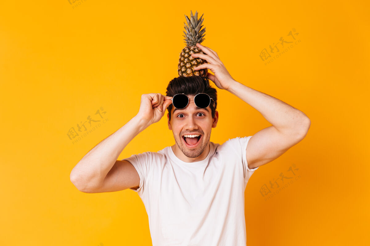 孤独棕色眼睛的淘气男人摘下太阳镜 把菠萝放在头上朋友身体阳刚