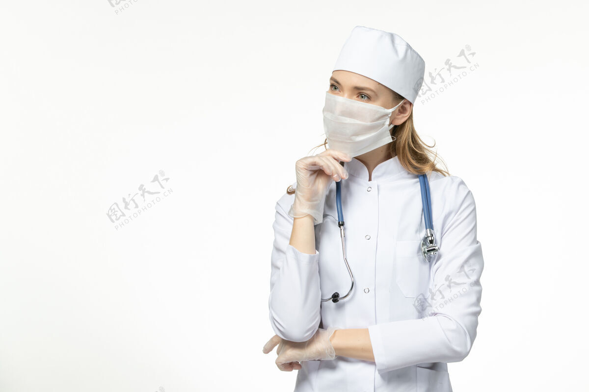浅白色正面图女医生穿着医疗服戴着口罩和手套因冠状病毒思考轻白壁病大流行冠状病毒大流行疾病手套