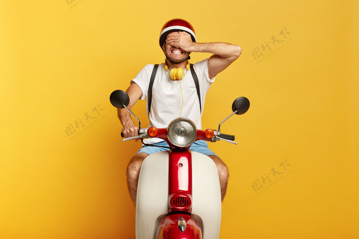 交通工具年轻人有自己的交通工具 骑着滑板车 用手掌遮住眼睛 穿着休闲服 隔离在黄色背景下隐藏骑手耳机