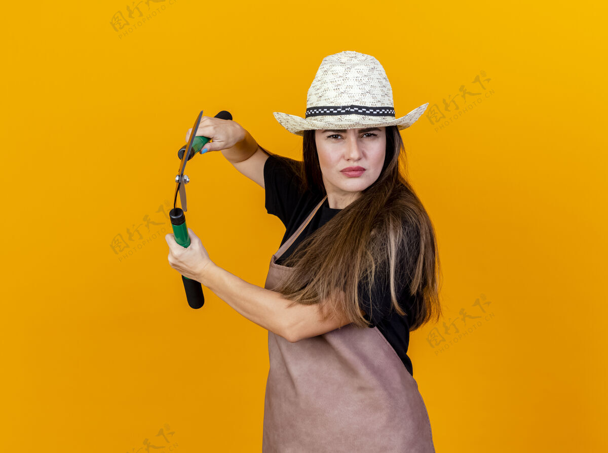 制服自信美丽的园丁女孩穿着制服 戴着园艺帽拿着剪子孤立在橙色信心花园剪子