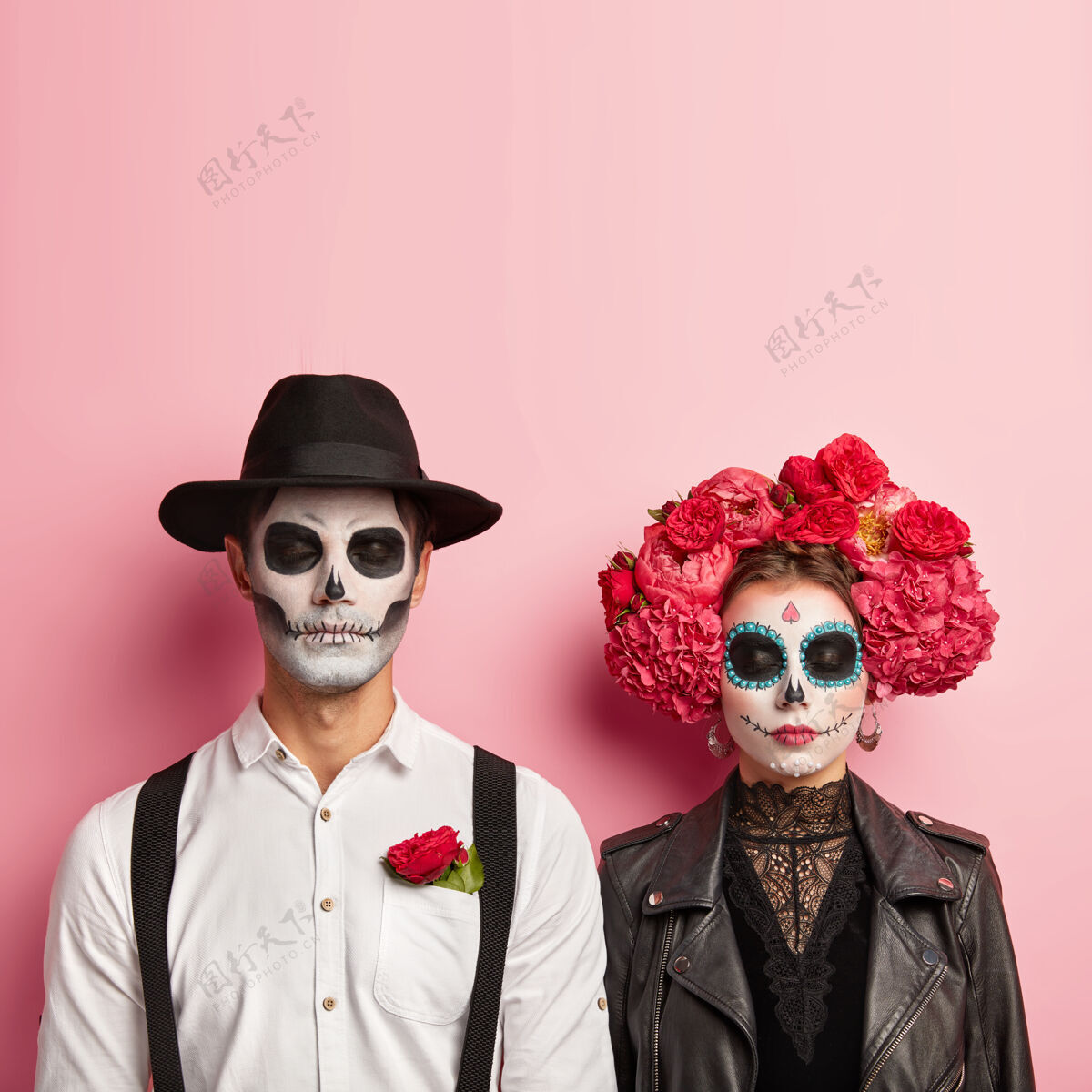 粉色可爱的情侣万圣节穿僵尸装 化头骨妆 男人戴帽子和口袋里插着红玫瑰的白衬衫 女人穿着黑色皮夹克和花环 一起等派对女人年轻浪漫