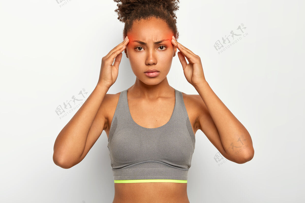 健康严重紧张的非裔美国妇女患有太阳穴疼痛 偏头痛 长期体育锻炼后精疲力尽 穿着上衣 对着白色的工作室墙摆姿势随意问题不高兴