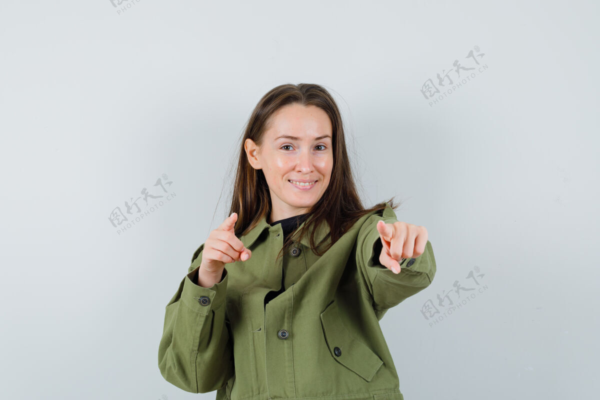 积极穿着绿色夹克的年轻女子指着前方 满意地看着前方女人年轻快乐