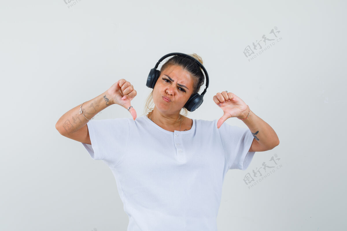 室内年轻的女士在听音乐 展示双拇指在t恤衫 前视图优雅正面双人
