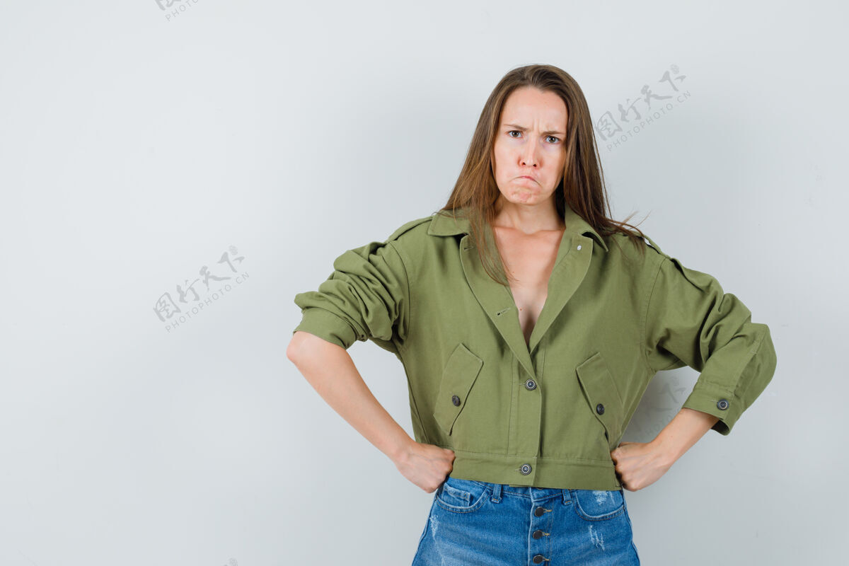 成人穿着绿色夹克 短裤 腰上握着拳头的年轻女性看起来很紧张正面图年轻黑发时尚