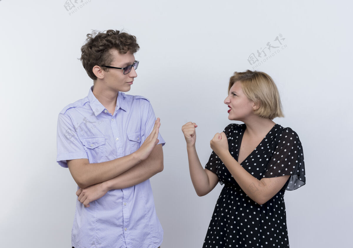表演年轻漂亮的夫妇愤怒的女人紧握拳头看着她困惑的男友 在白墙上显示停止的手势男朋友手势表情