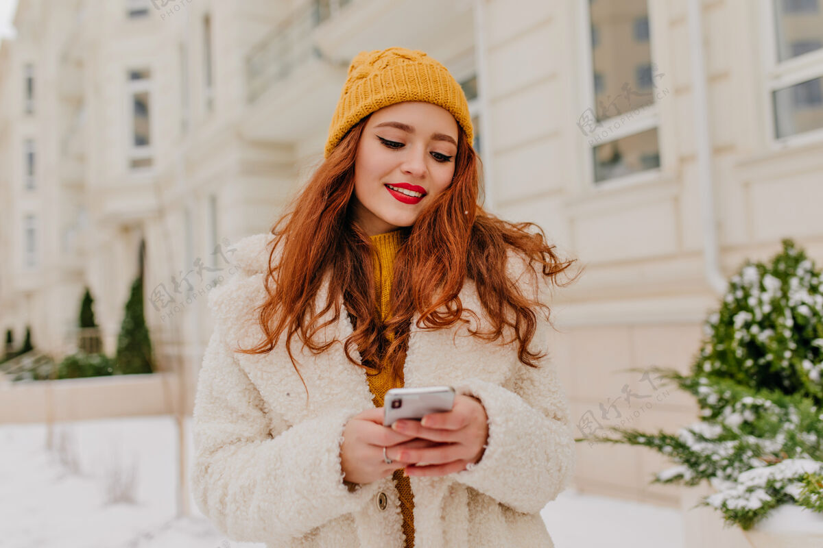 城市美丽的红发女孩在发短信冬天穿着外套的年轻女子和手机合影的户外照片冻结笑云杉
