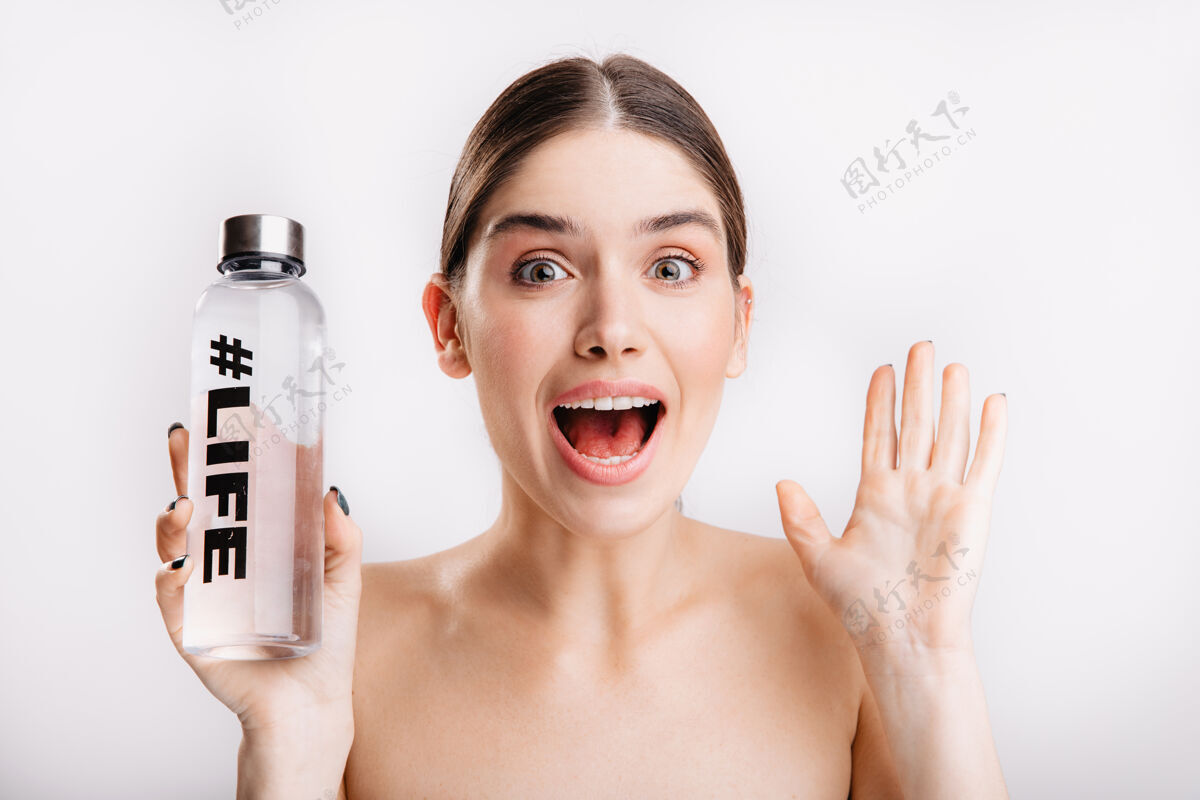眉毛皮肤干净健康的惊讶女孩的画像女士惊奇地摆出姿势 手里拿着一瓶写着生命的水成人画像清洁