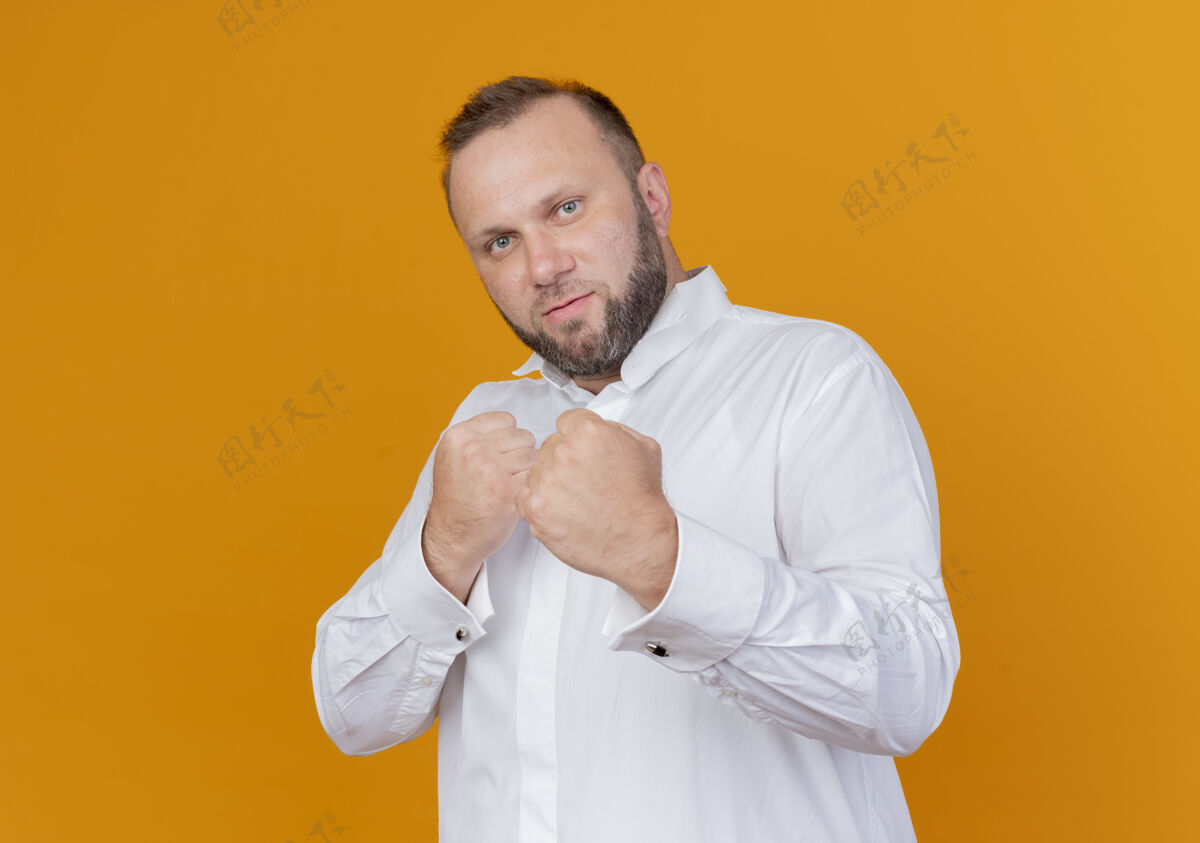 握紧留着胡子的男人穿着白衬衫 握紧拳头 像个拳击手站在橘色的墙上拳头胡子拳击手