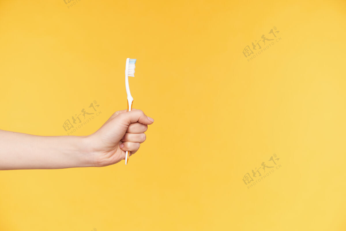 护理皮肤白皙的女士举起的手紧握着手指的水平照片白色牙刷在橙色背景上摆姿势牙齿护理概念手黄色牙刷