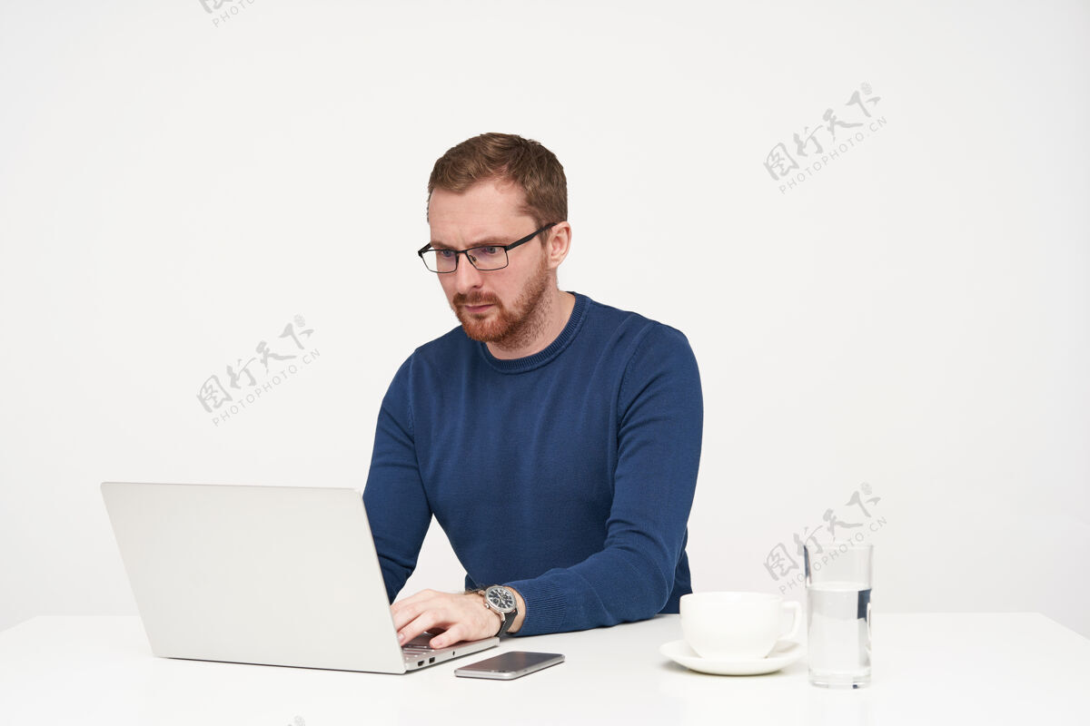 毛衣室内镜头：戴着眼镜 留着胡须的年轻人一边认真地看着笔记本电脑的屏幕 一边工作 一边把手放在键盘上 与白色背景隔离开来年轻人水姿势