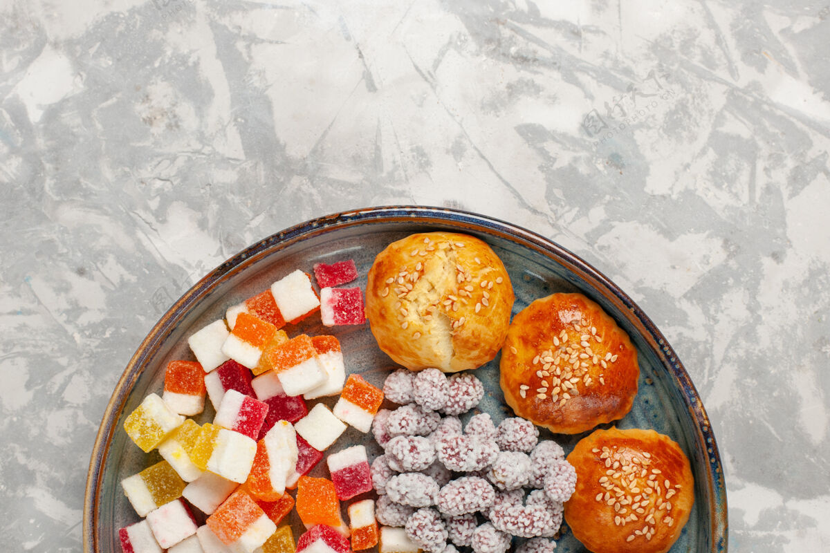 盘子顶视糖糖果与小甜面包在淡白色的表面蔬菜晚餐饮食