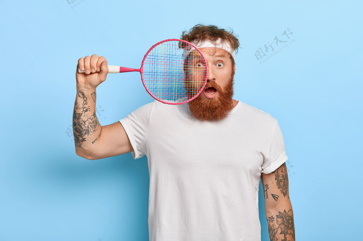 人一个被吓坏了的红发网球运动员拿着球拍对着蓝色的墙摆姿势的水平镜头比赛红发人