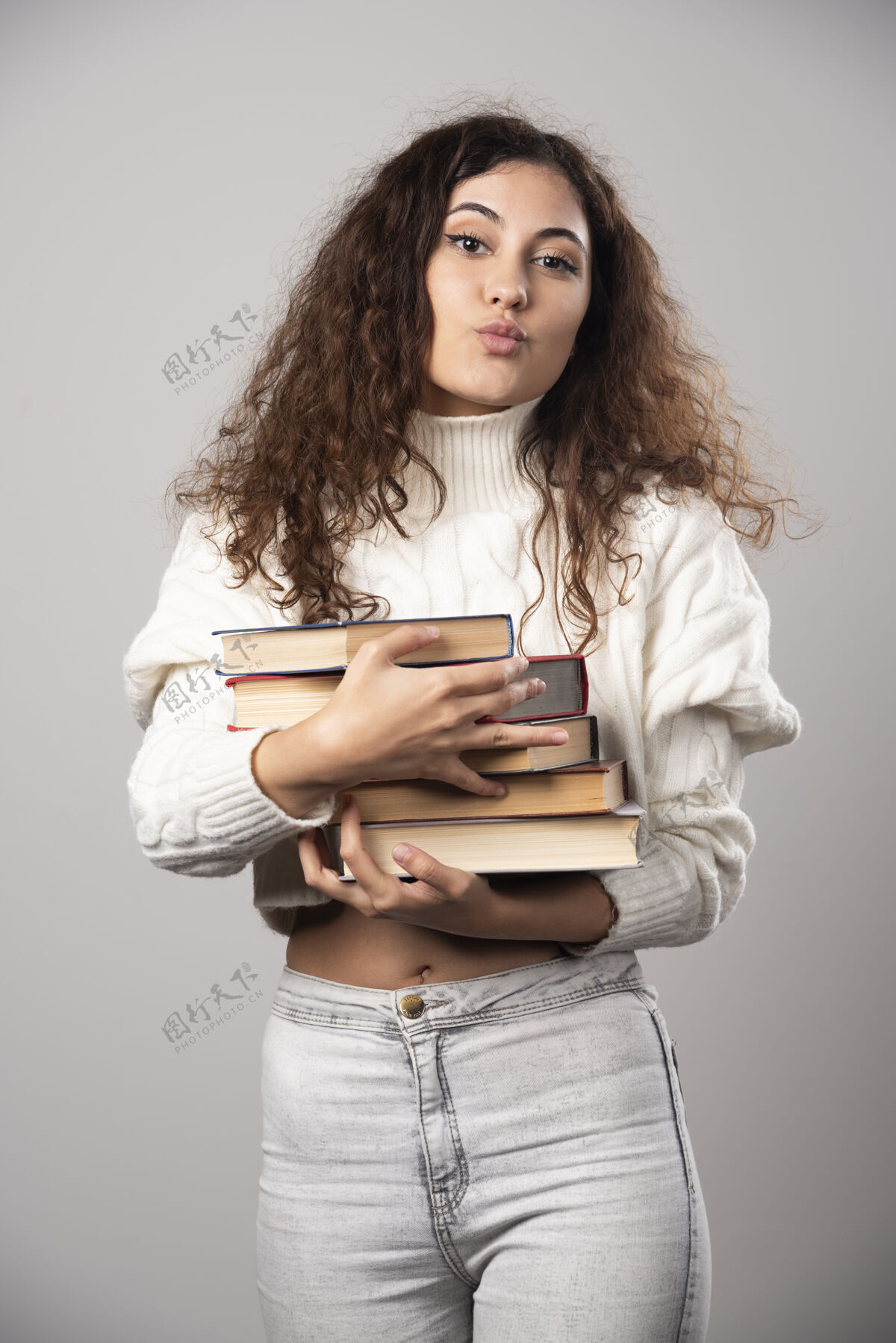 女士一个年轻女子拿着一堆书在灰色的墙上高质量的照片人女性年轻