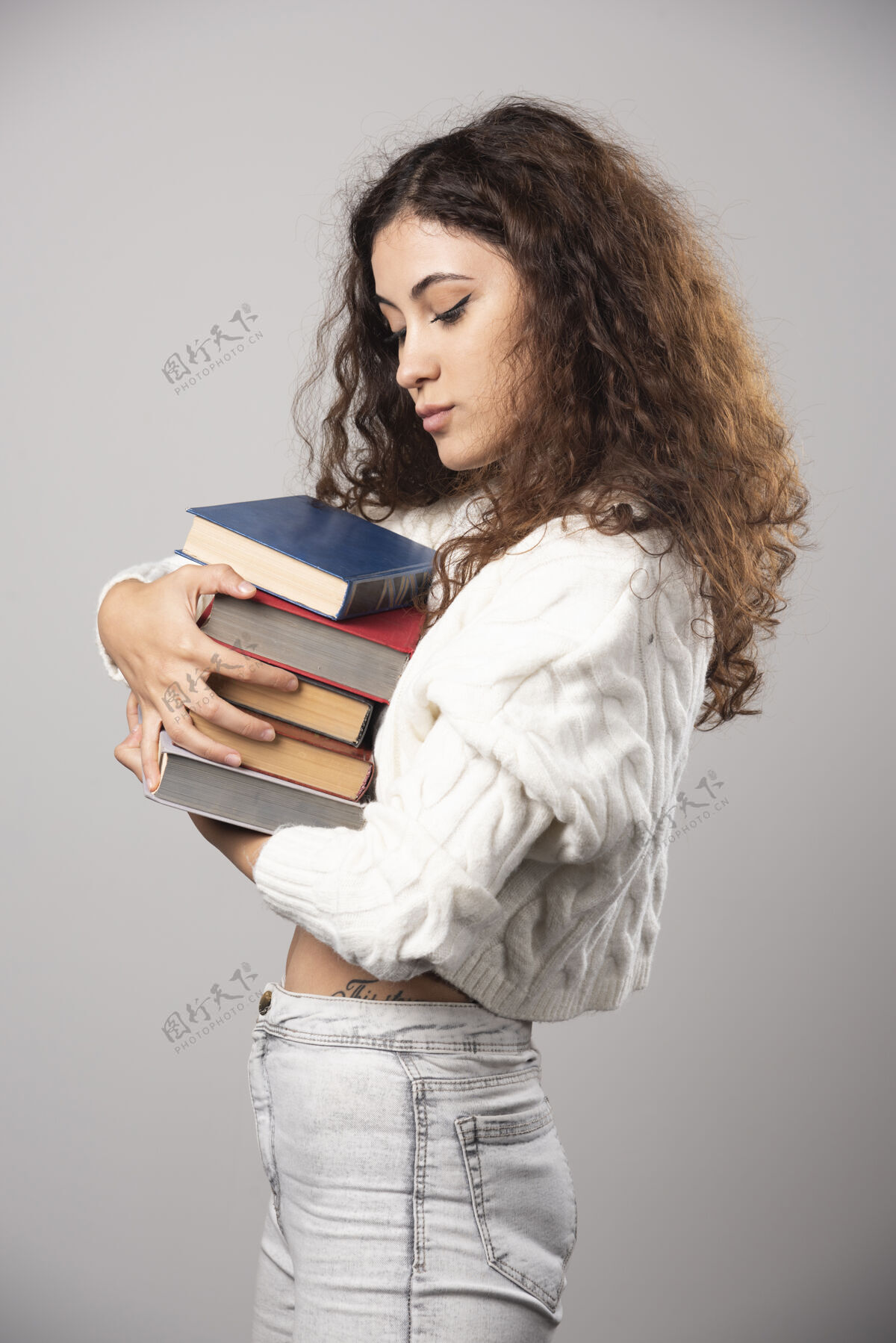 微笑一位年轻的女士在灰色的墙上展示一堆书高质量的照片人女孩女性