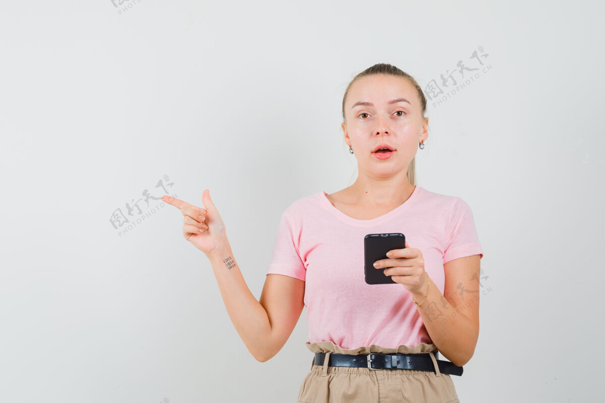 时尚金发女孩拿着手机 指着旁边的t恤 裤子前视图旁白美丽时尚