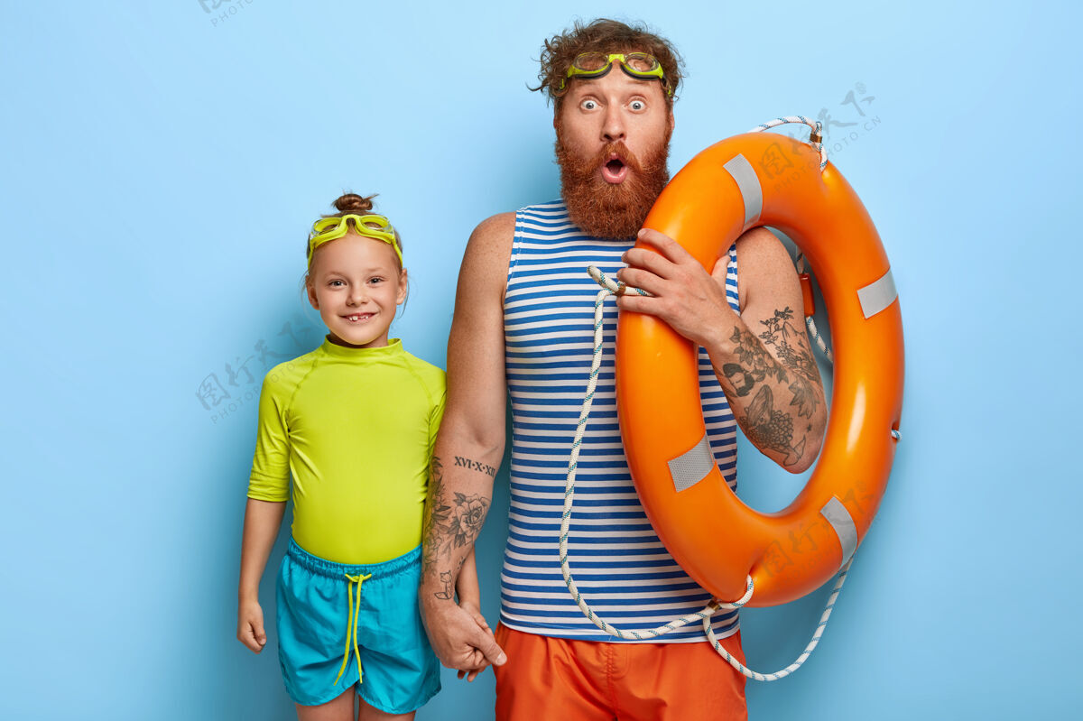 童年姜黄色胡须的震惊父亲的水平镜头 戴着护目镜 拿着救生圈 小女孩儿和爸爸一起度过空闲时间 去学习在蓝色墙壁上游泳夏天的时间娱乐游泳休息