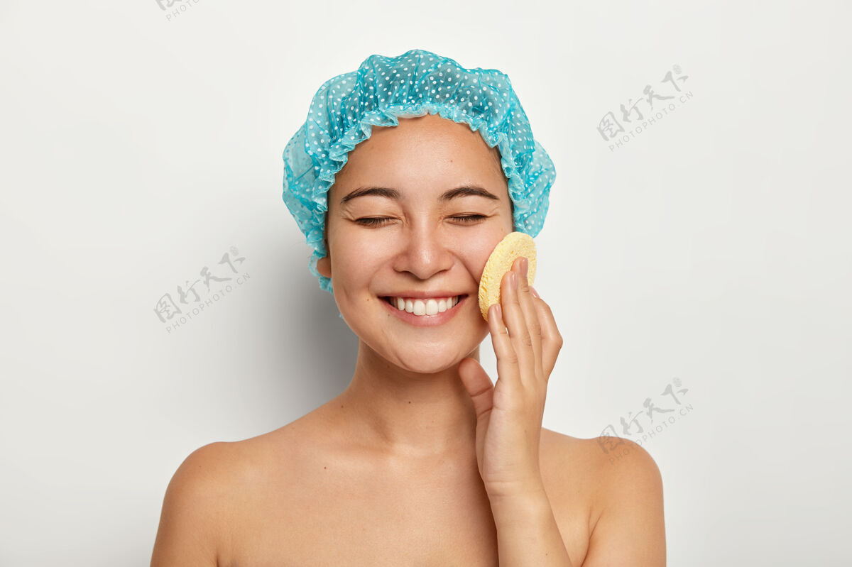 健康美容可掬的笑脸美女写真用化妆海绵洁面 赤裸着站在白色的墙壁上 想要拥有完美的肌肤面部护理 spa程序理念美容牙齿室内