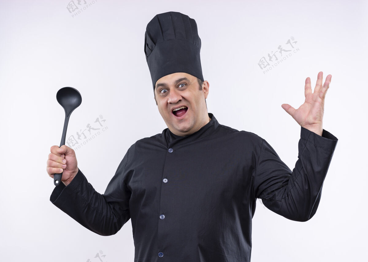穿男厨师身穿黑色制服 头戴厨师帽 举着勺子 举着胳膊 站在白色背景下 用咄咄逼人的表情看着镜头厨师看着手臂