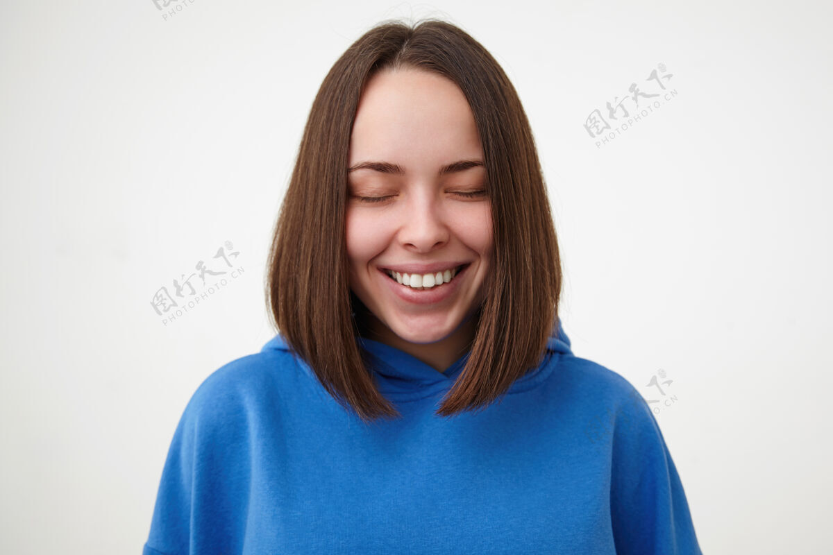 模特可爱的年轻快乐的棕色头发的女人 留着鲍勃式的发型 闭着眼睛 快乐地微笑着 穿着运动服 在白色的墙上摆姿势肖像姿势情绪