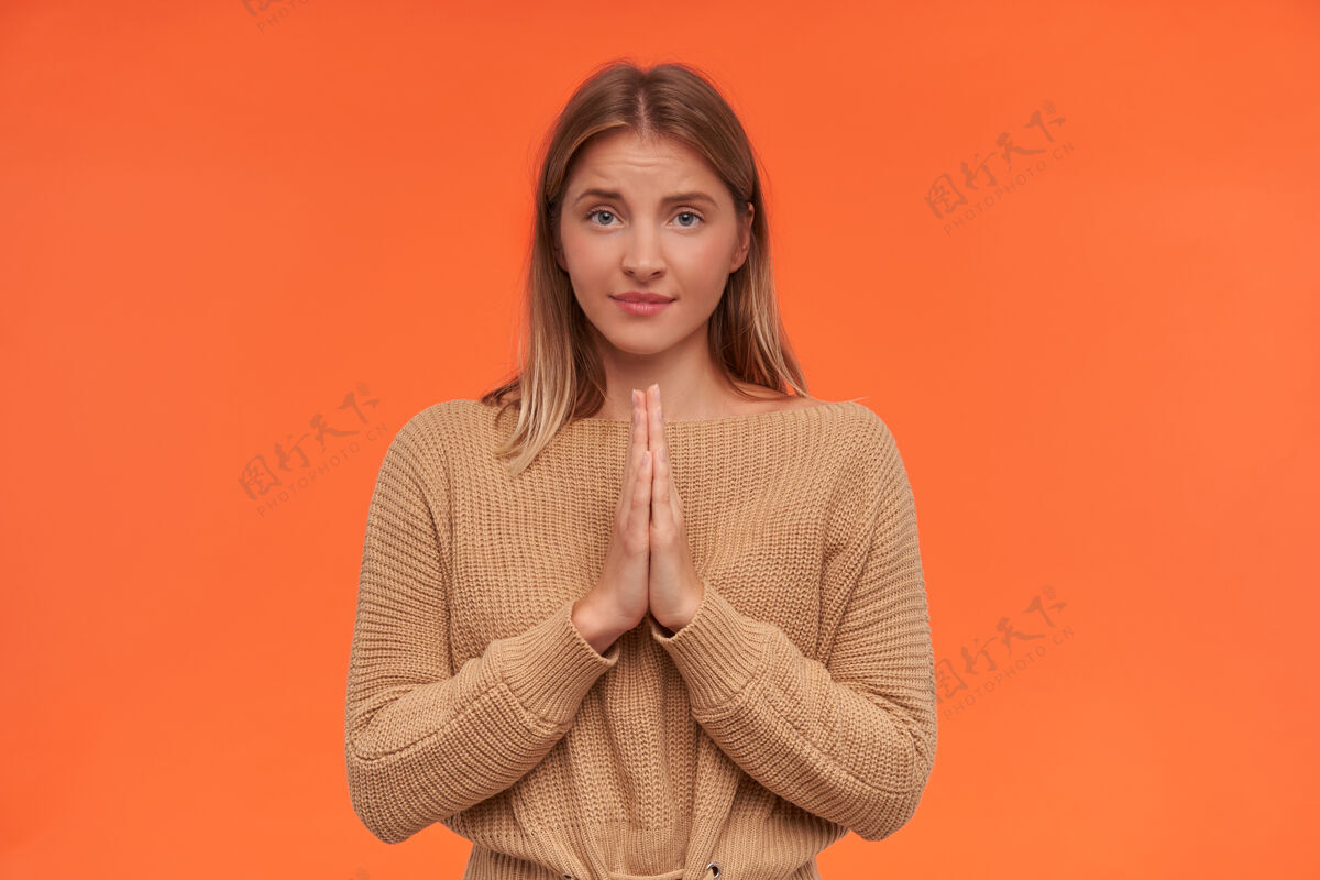 化妆品室内拍摄的年轻困惑的白头女士与自然化妆形成举手祈祷的姿态 而站在橙色的墙壁手势针织宽松