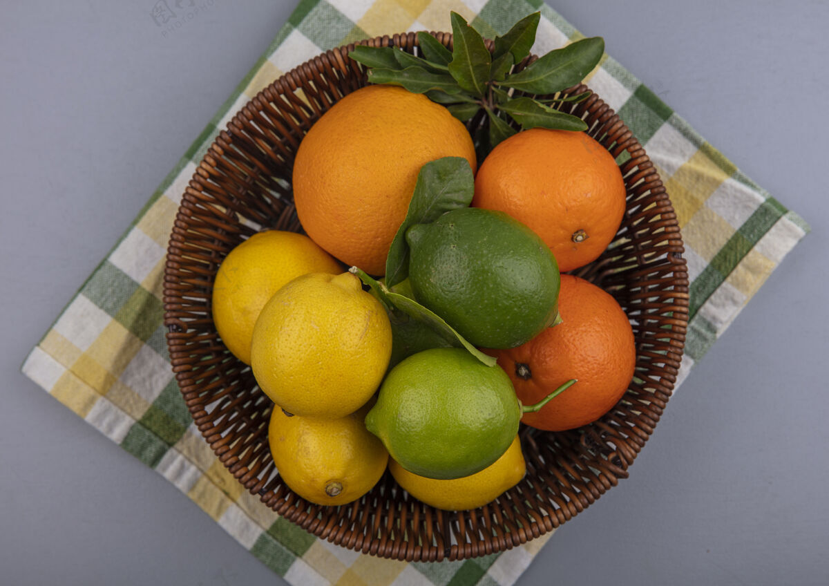 灰色在灰色背景下 黄色格子毛巾上的篮子里放着柠檬和酸橙的橙子格子黄色视野