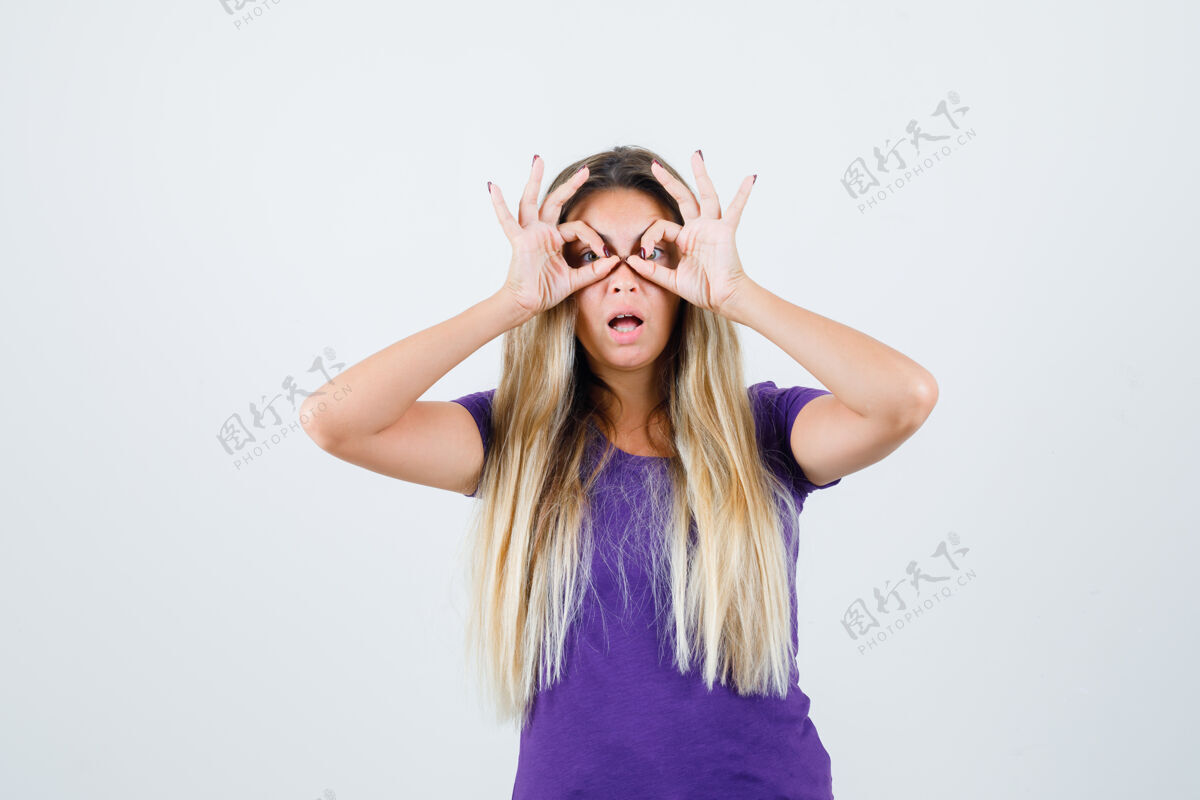 时尚身着紫罗兰色t恤的金发女人展示眼镜姿势 看上去很惊讶 正面视图年轻成人手